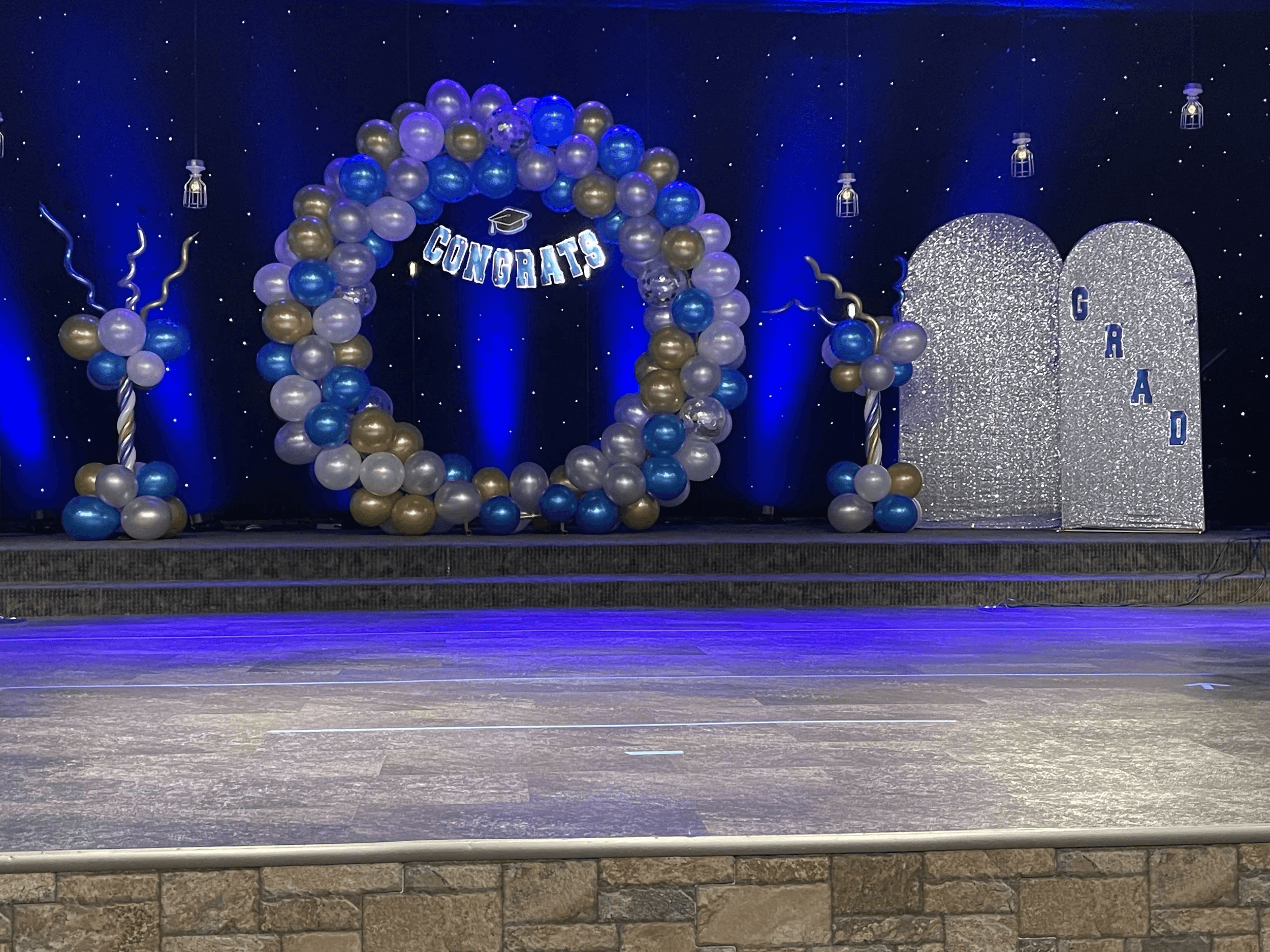 Blue and gold graduation balloon arch with Congrats banner on a stage